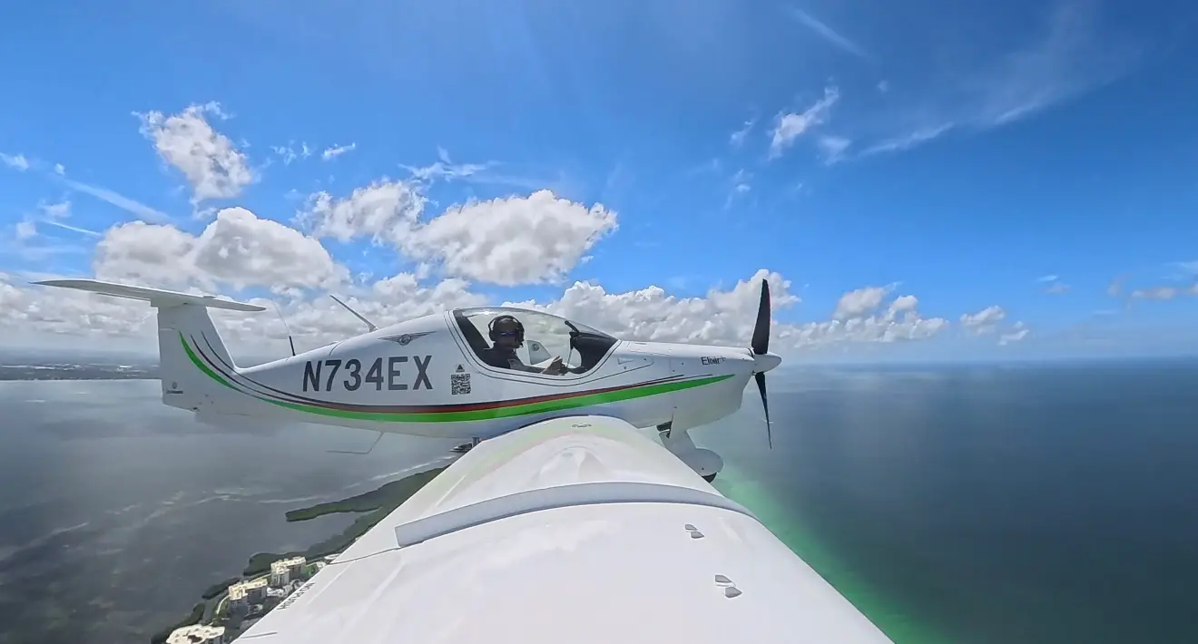 Elixir Aircraft N734EX flying over water, side view wing