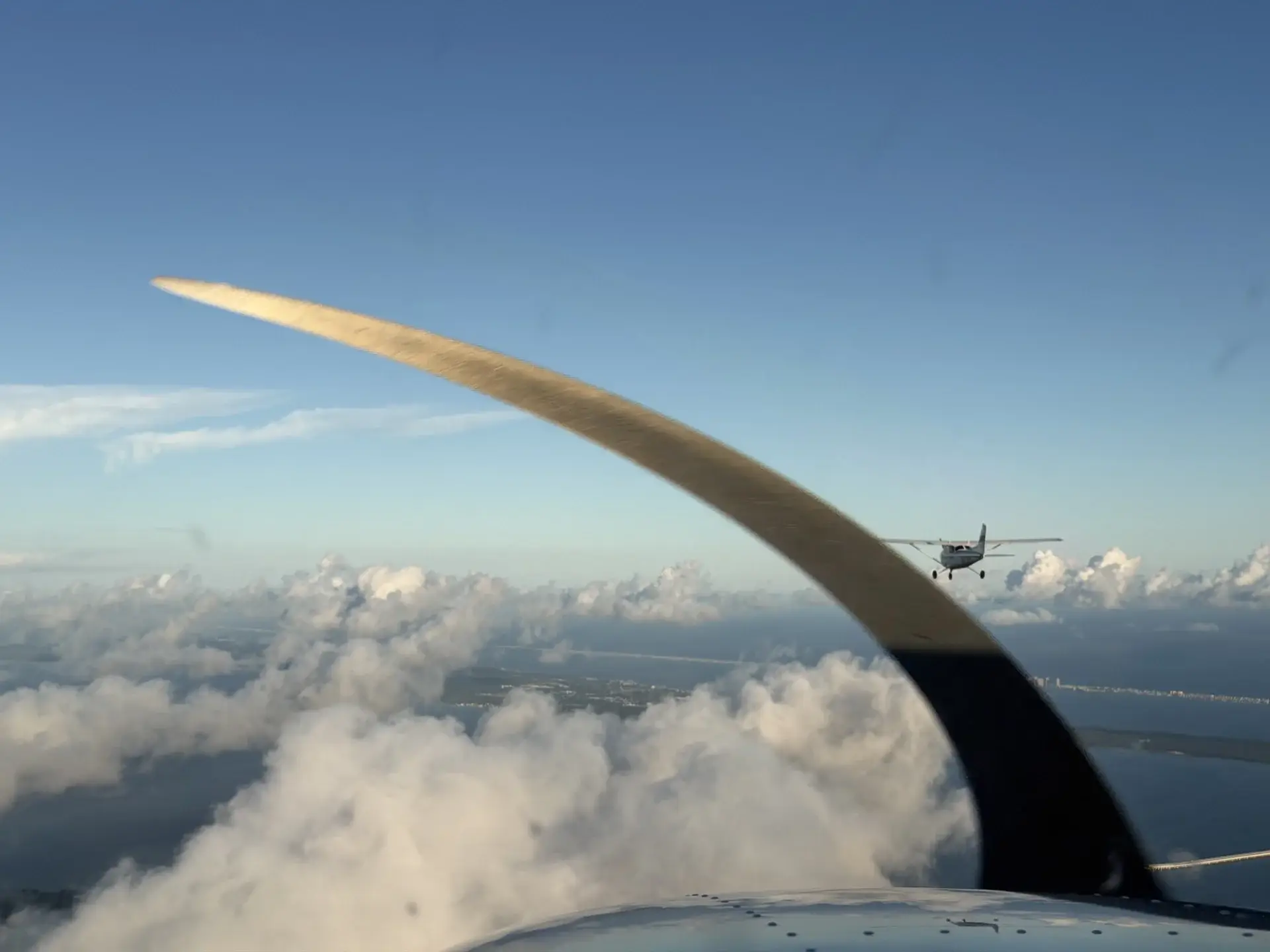 Plane flying over clouds seen through turbine with another plane in the distance