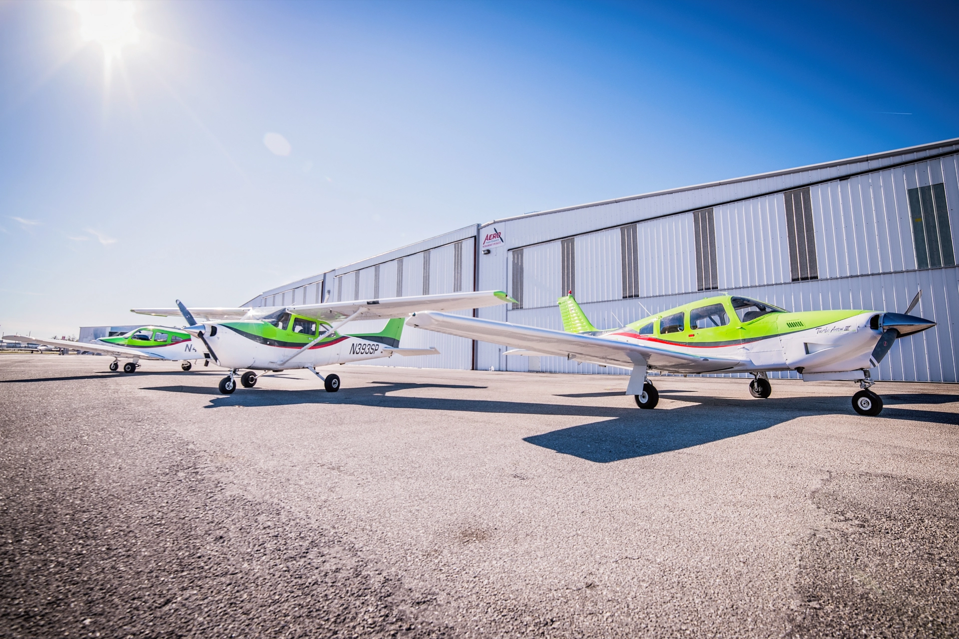 Cessna 172 and Piper training airplanes parked in front of a hangar on a sunny day