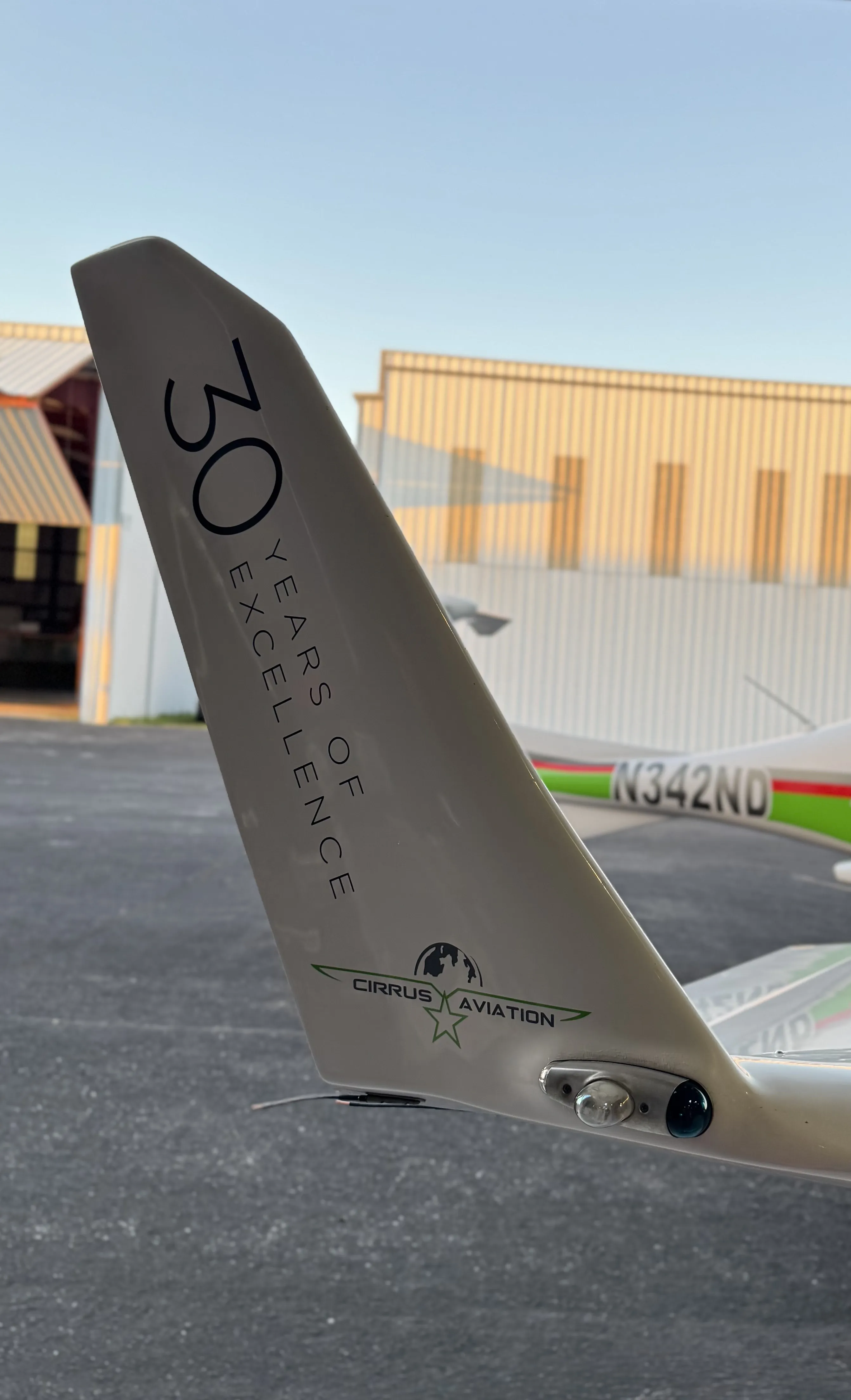 Aircraft tail with 30 Years of Excellence lettering in front of the Cirrus Aviation hangar at sunset