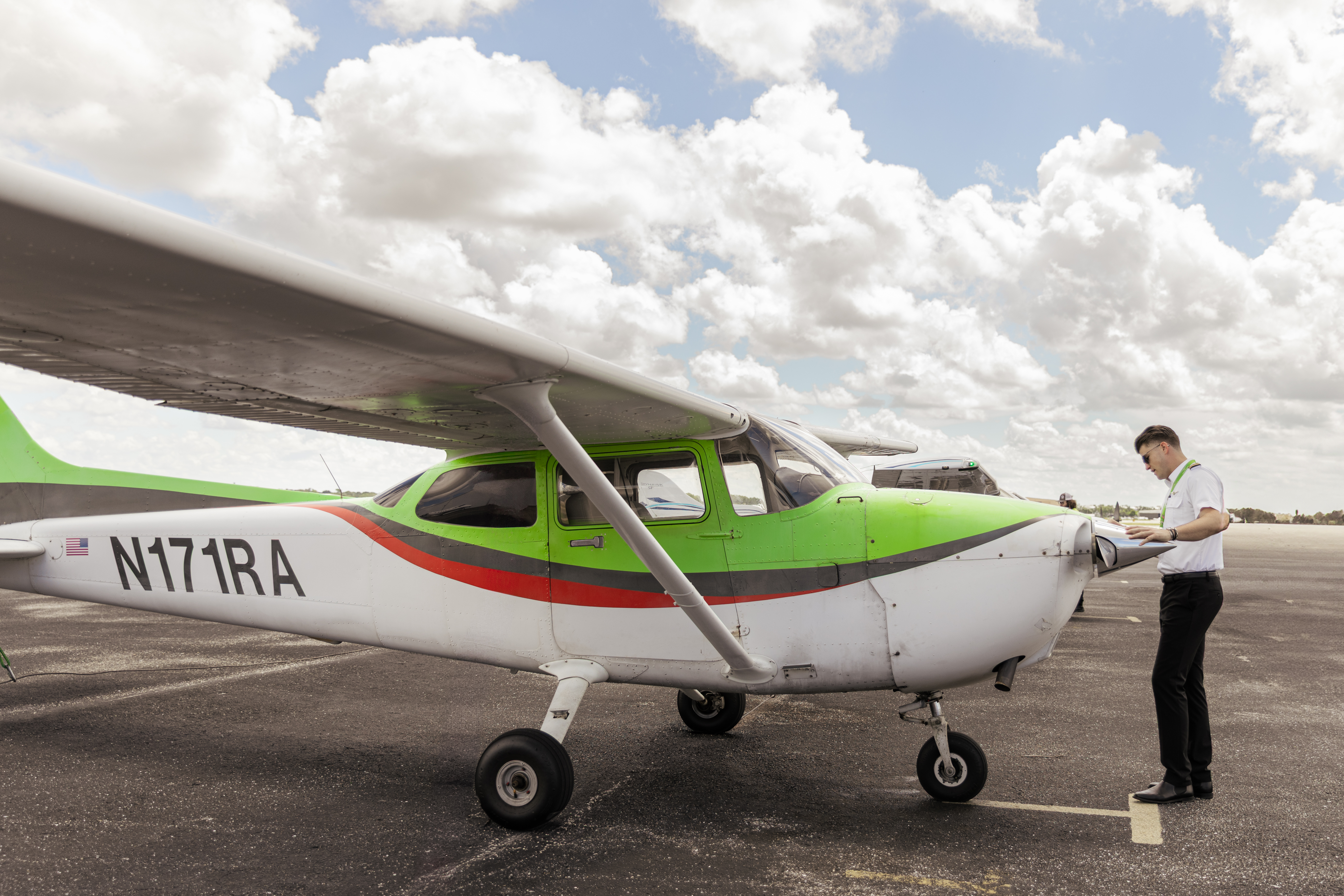 Pilot standing at the nose of Cessna 172 Skyhawk N171RA under its high wing on the Cirrus Aviation ramp