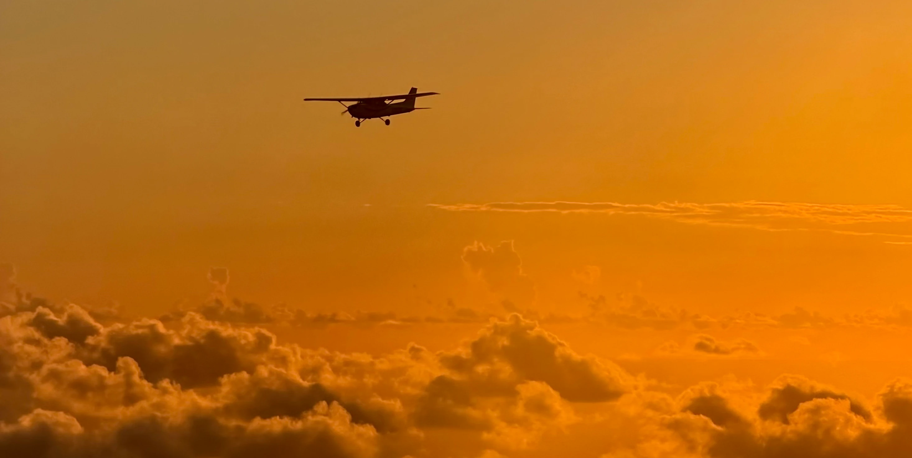 Cessna airplane flying in the distance over clouds during sunset