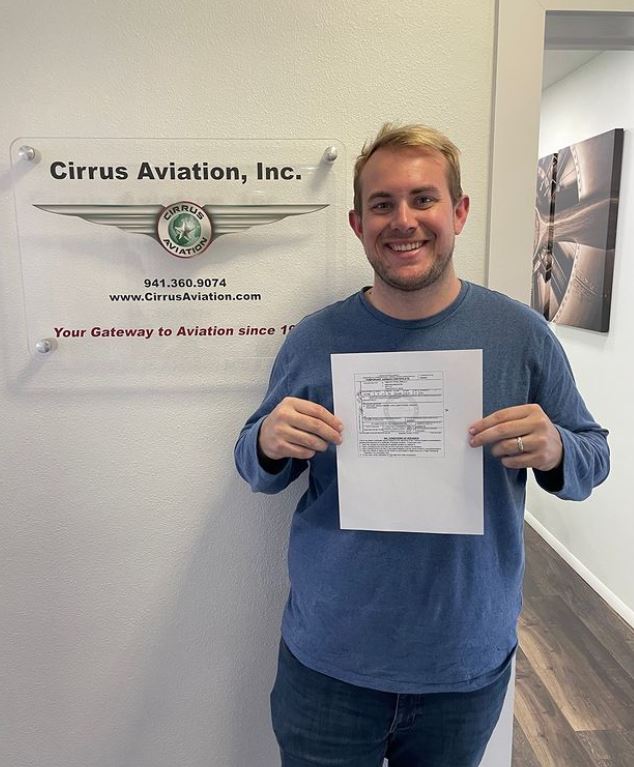 Student holding a certificate and smiling at the camera inside Cirrus Aviation's office