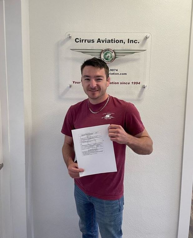 Student holding a certificate and smiling at the camera inside Cirrus Aviation's office